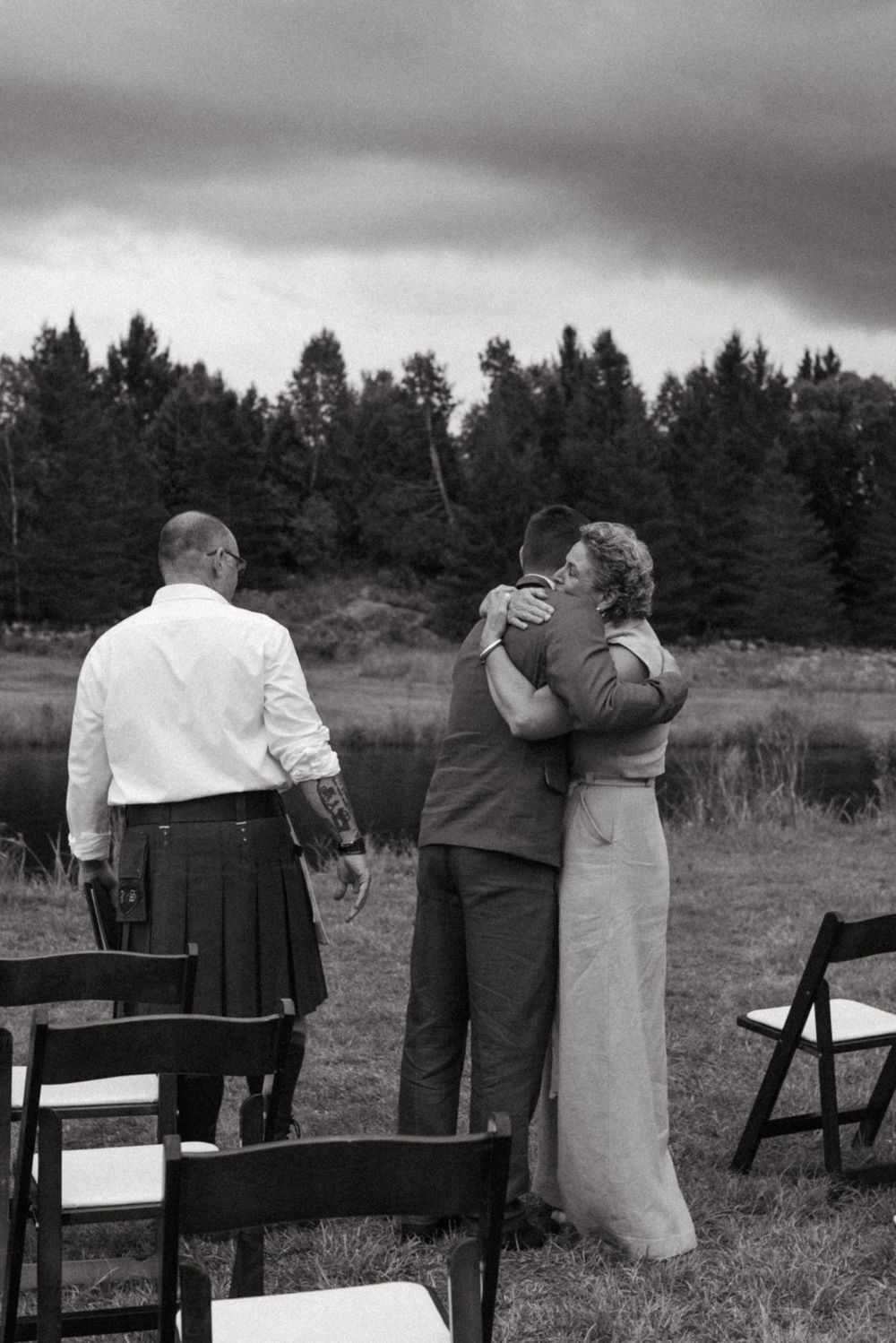 A series of black and white photos showing couples embracing while standing in a field with pine trees in the background.