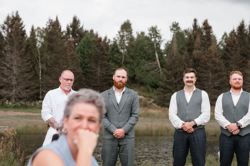 A series of outdoor wedding party photos showing groomsmen in gray suits posing by a lake with evergreen trees in background.