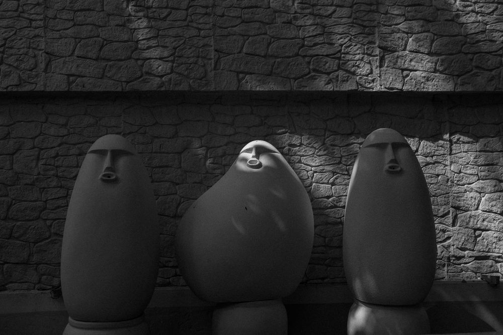 A row of dark silhouetted pumpkins sits against a textured stone wall in dramatic lighting.