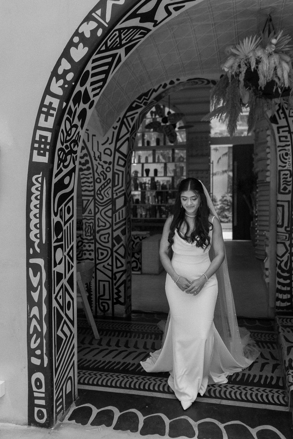 A black and white photo series showing a person in a white dress posing under decorative arches with tribal patterns.