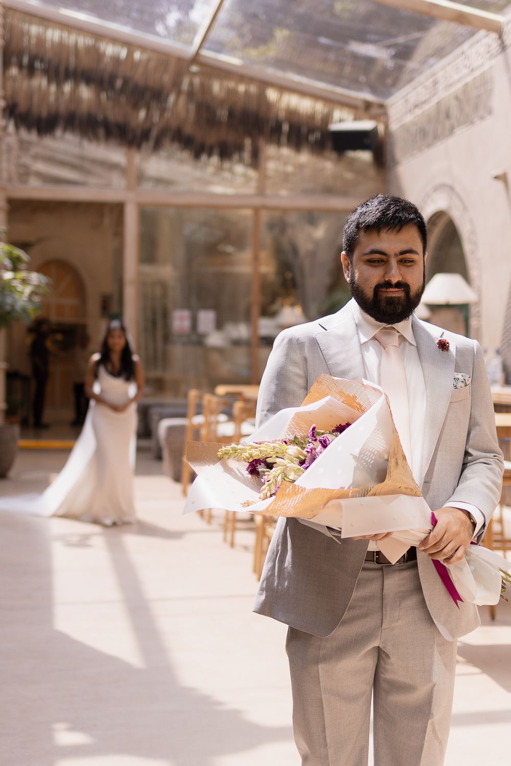 A sequence of photos showing a person in a light gray suit holding a bouquet while walking through a sunlit venue.