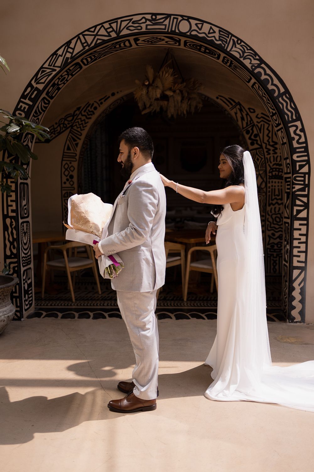 A couple in traditional white attire performs a ceremonial dance under ornate arched architecture with decorative patterns.