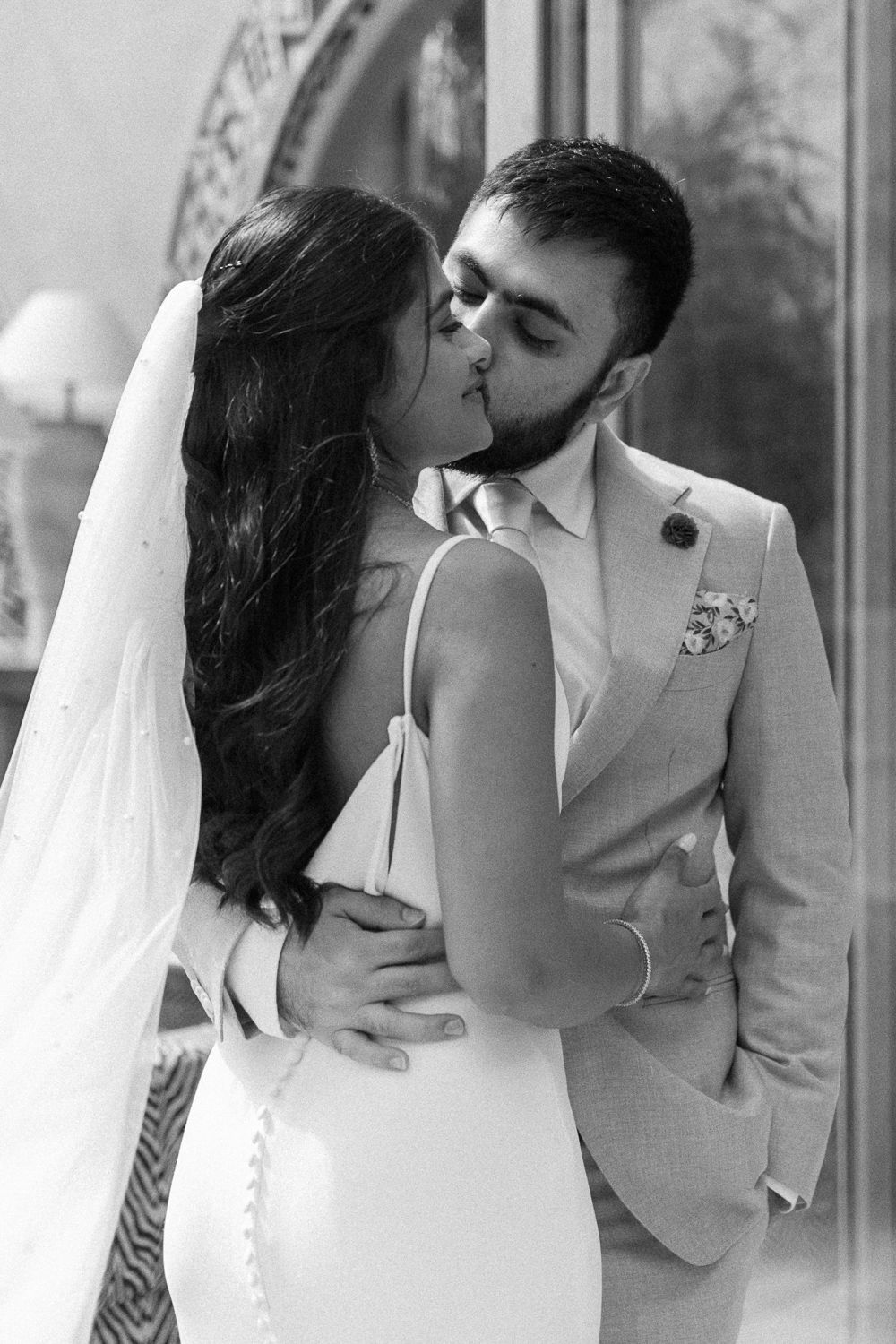 A romantic black and white wedding photo of a couple sharing a kiss, with the bride in a fitted white dress and veil.