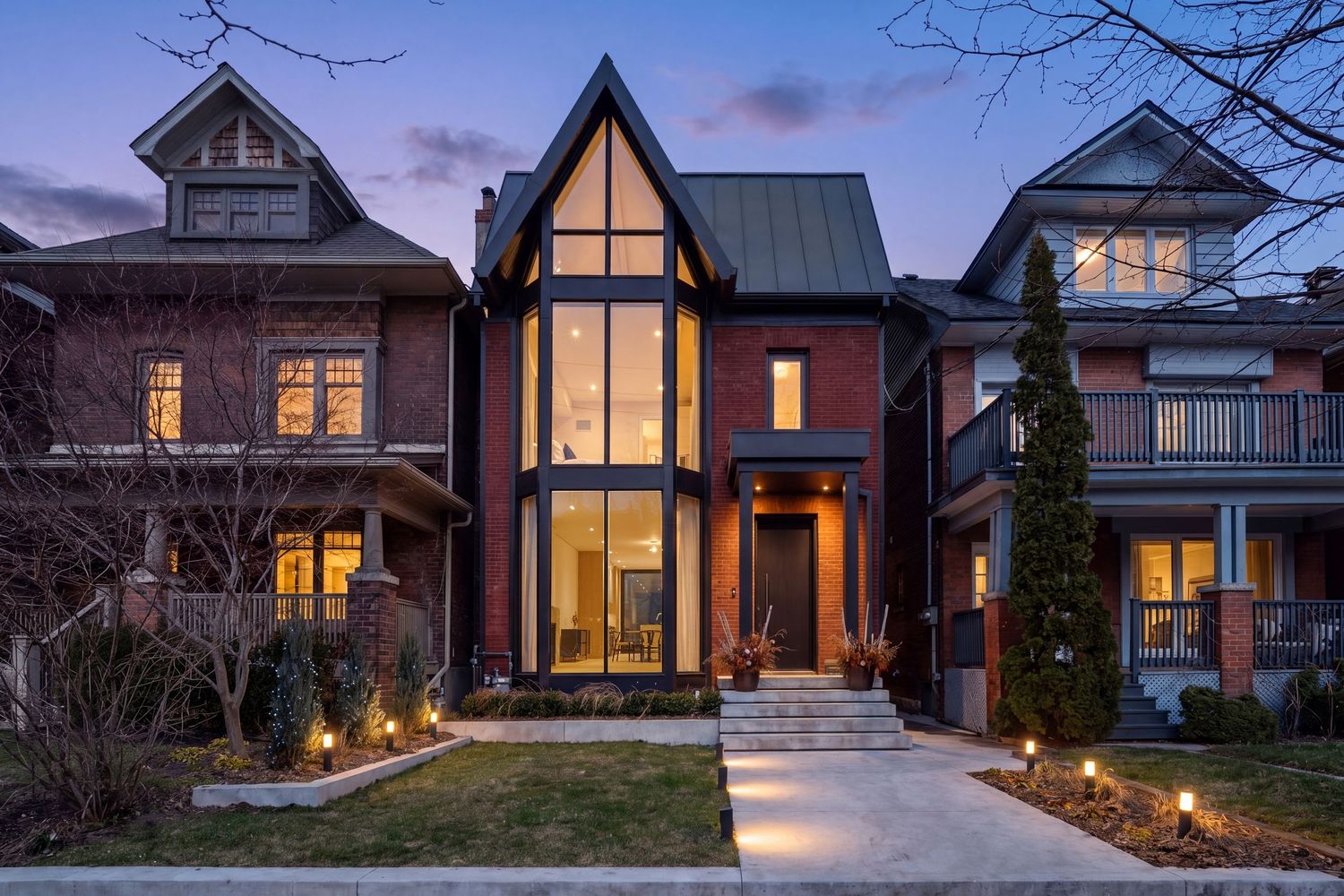Modern brick home with dramatic glass gable entrance, illuminated at dusk, blending contemporary and traditional architecture.