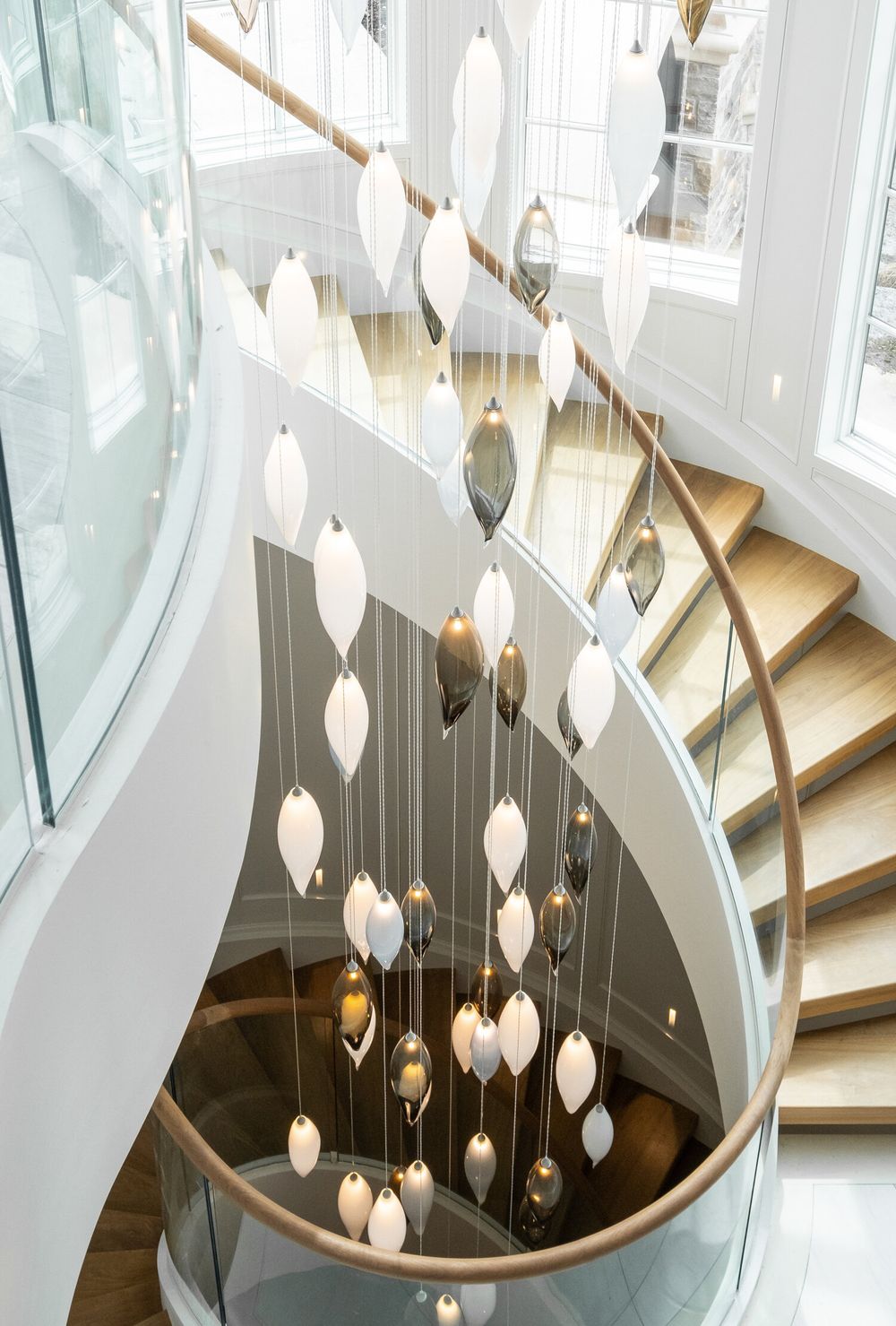 Modern spiral staircase with hanging diamond-shaped pendant lights creating an elegant lighting installation in white interior.