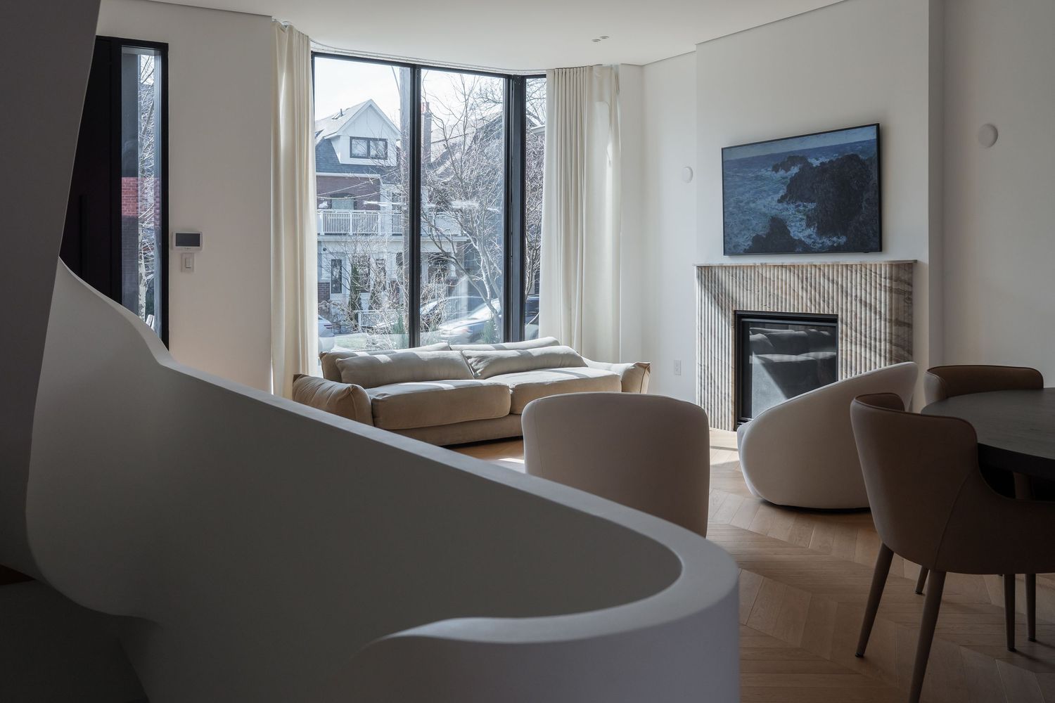 Modern living room with curved white staircase, marble fireplace, large windows, and neutral furniture in a contemporary home.