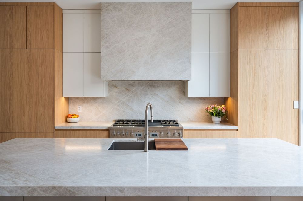 Modern kitchen with marble countertop, wood cabinets, stone backsplash, and stainless steel range with hood.