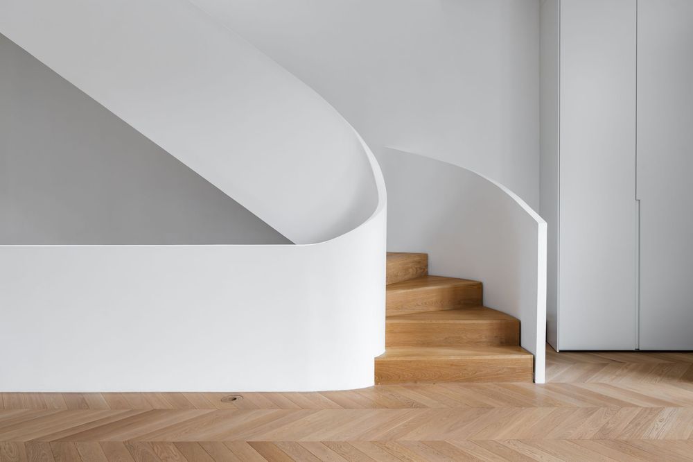 Modern staircase with curved white walls and natural oak wood steps on herringbone parquet flooring.