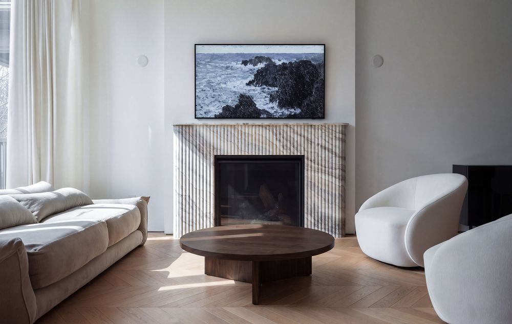 Modern living room with marble fireplace, dark wood coffee table, white curved chair, and beige sofa on herringbone parquet floor.
