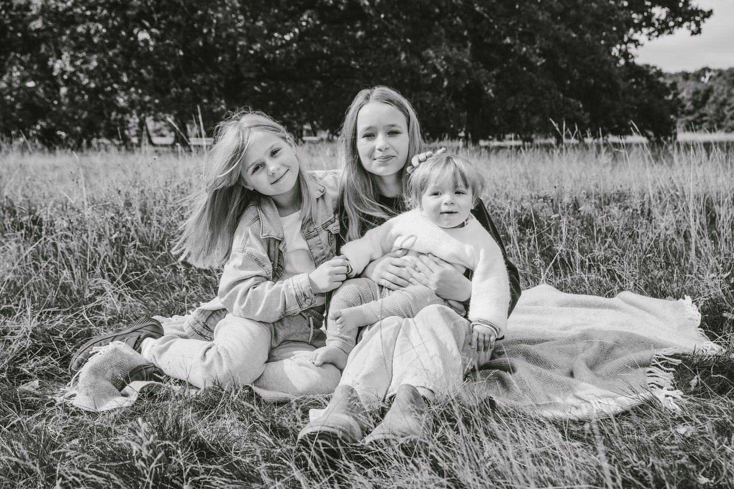 Black and white photo of a mother sitting in a field with her three young daughters, smiling warmly.