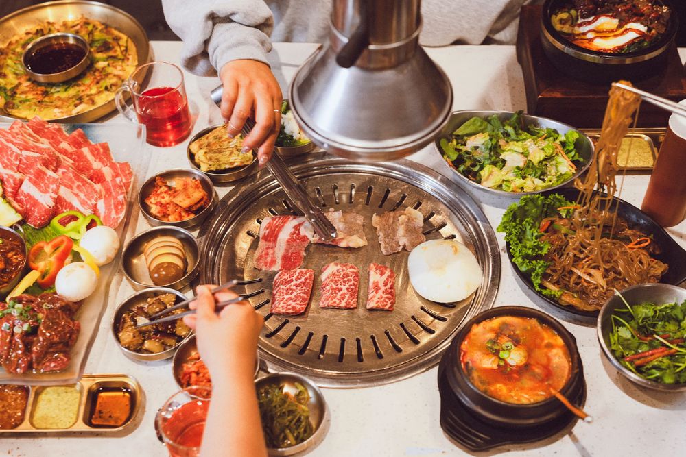 Korean BBQ table with grilling meat, banchan side dishes, soup, and salad spread for a traditional dining experience.
