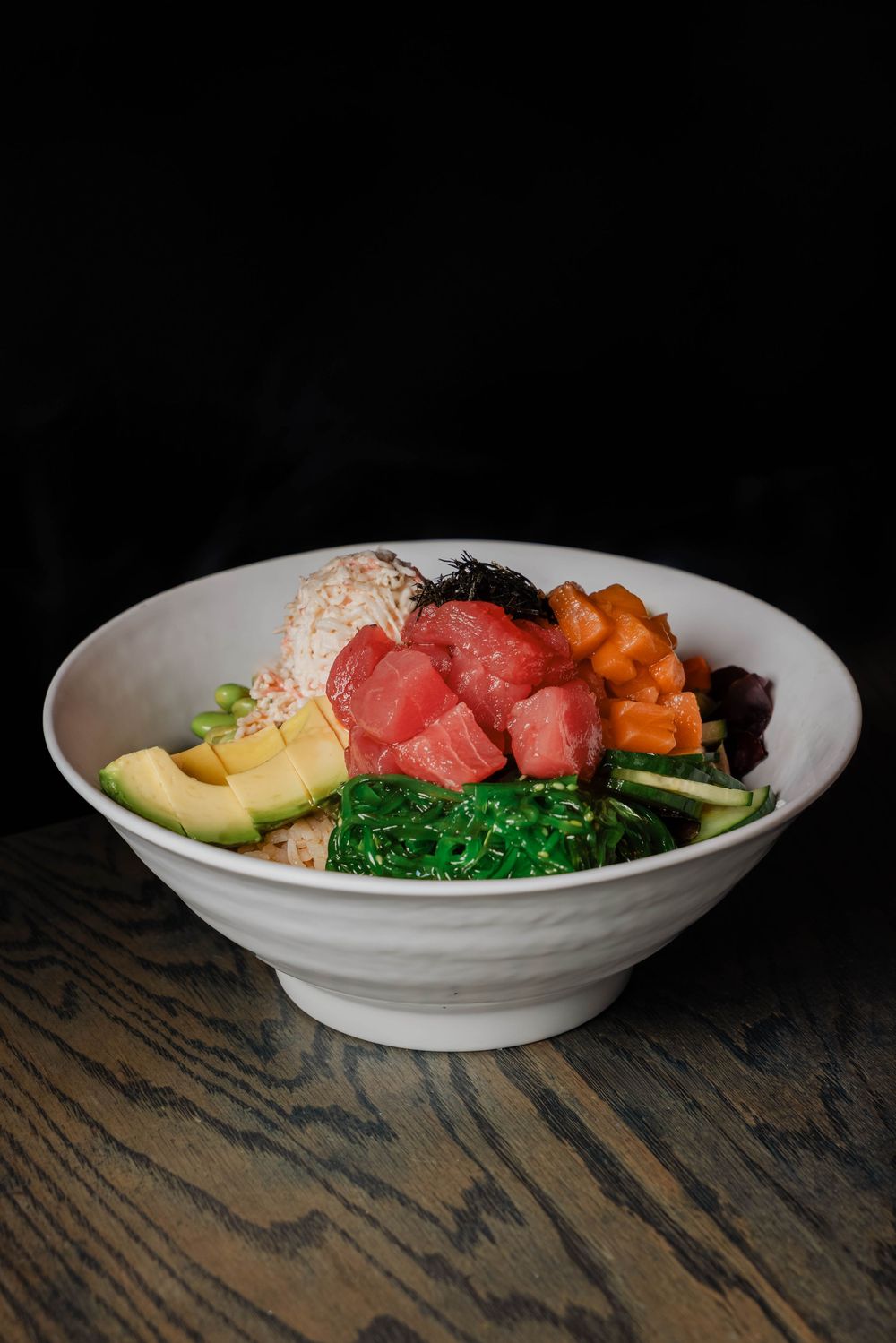 Fresh tuna poke bowl with avocado, seaweed salad, cucumber, carrots, and rice in a white ceramic bowl.