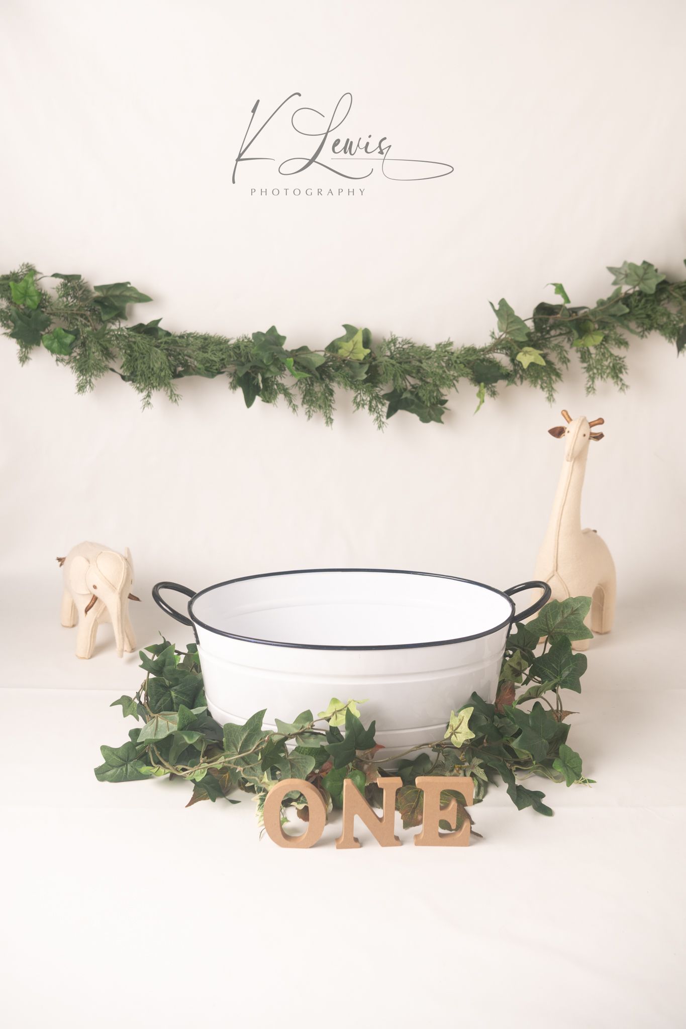 First birthday cake smash setup with white enamel tub, wooden ONE letters, ivy garland, and toy animals by K Lewis Photography.