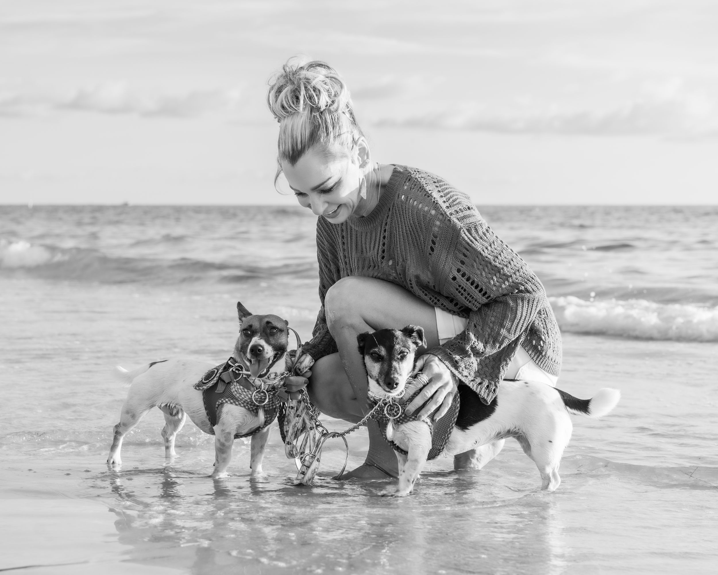 Woman crouching with three small dogs on a beach in black and white photo.