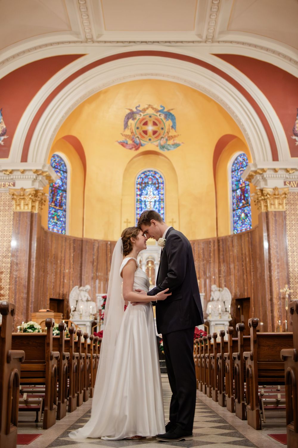 Bride and groom share an intimate moment at the altar of a beautiful church with stained glass windows.