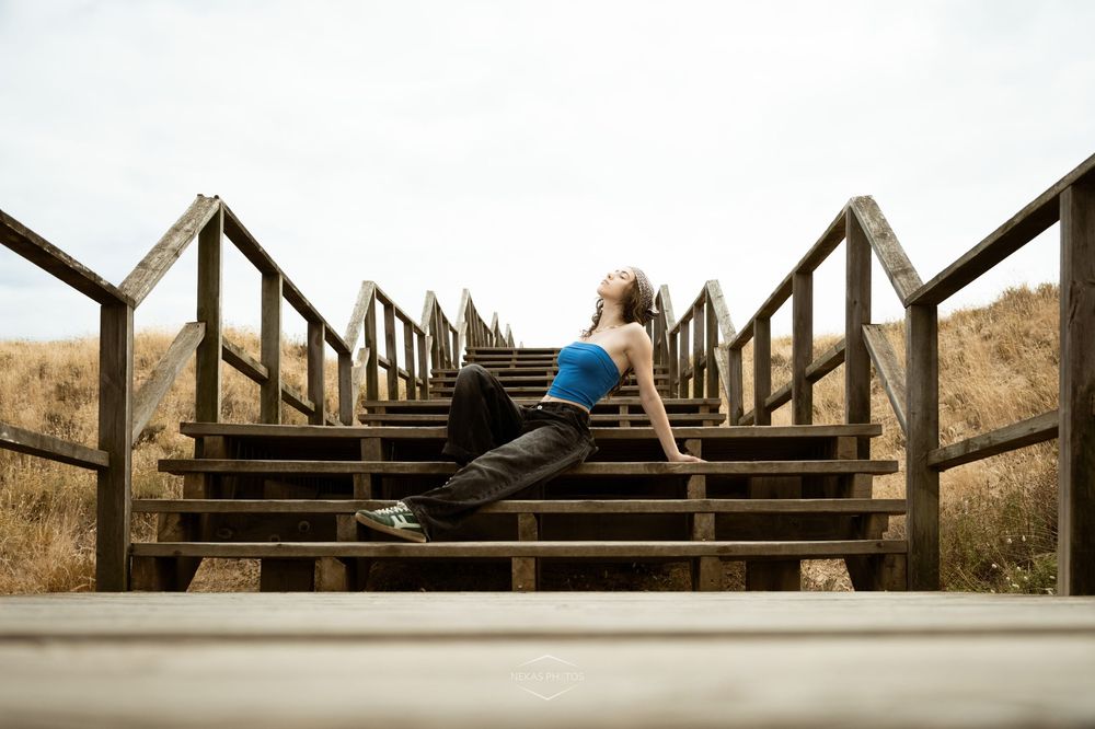 Woman in blue top sitting on wooden outdoor stairs, resting after a workout with scenic dry grass background.