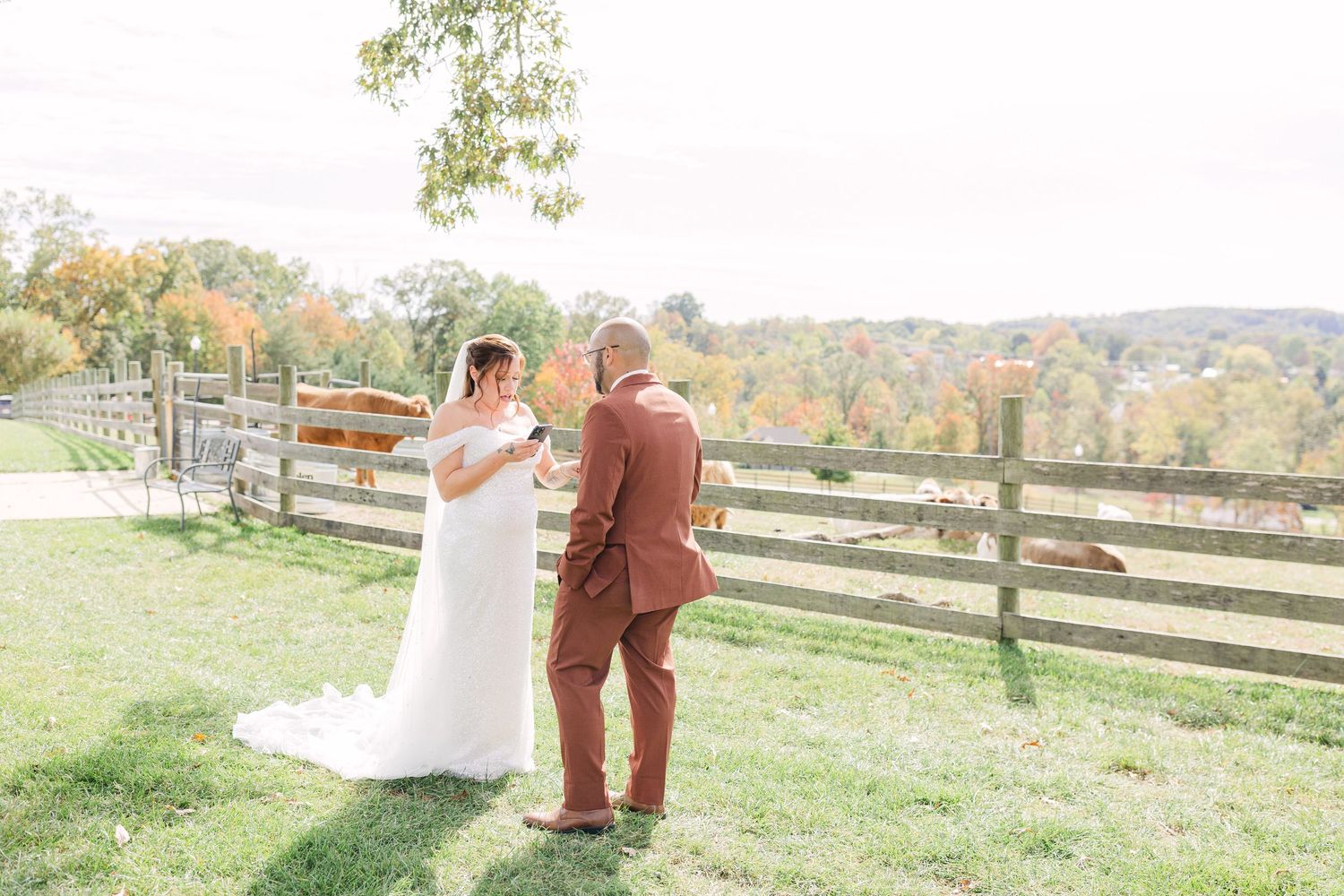Bride and groom share a first look moment outdoors by a wooden fence with fall foliage backdrop.