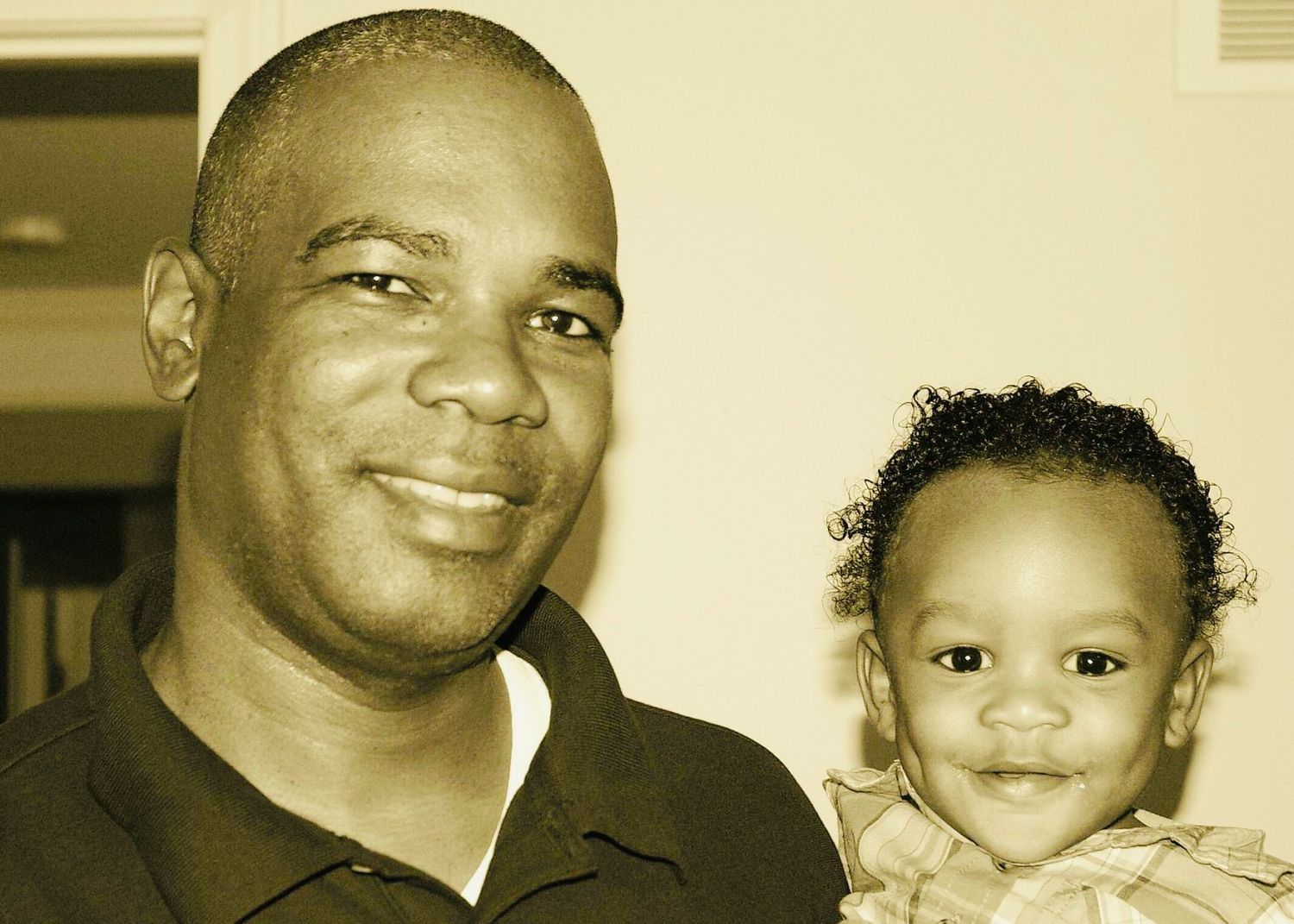 Smiling man posing with a happy toddler in a warm sepia-toned portrait photo.