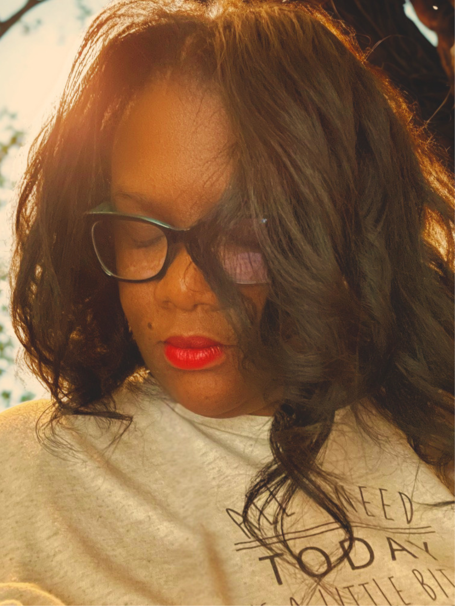 Young woman with glasses and red lipstick wearing a gray sweatshirt, photographed in warm sunlight.