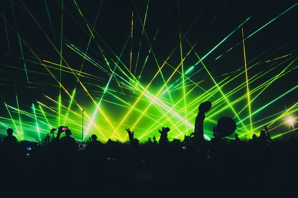 Green laser light show illuminates a massive crowd at an electrifying nightclub or music festival concert.