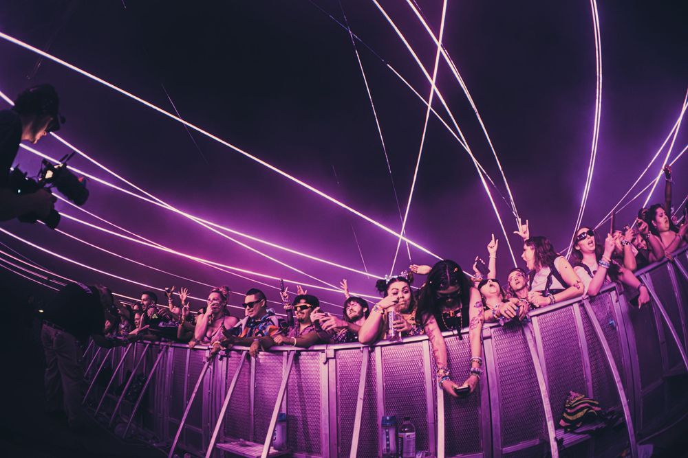 Crowd of concert fans cheering under vibrant purple laser lights at an energetic live music event.