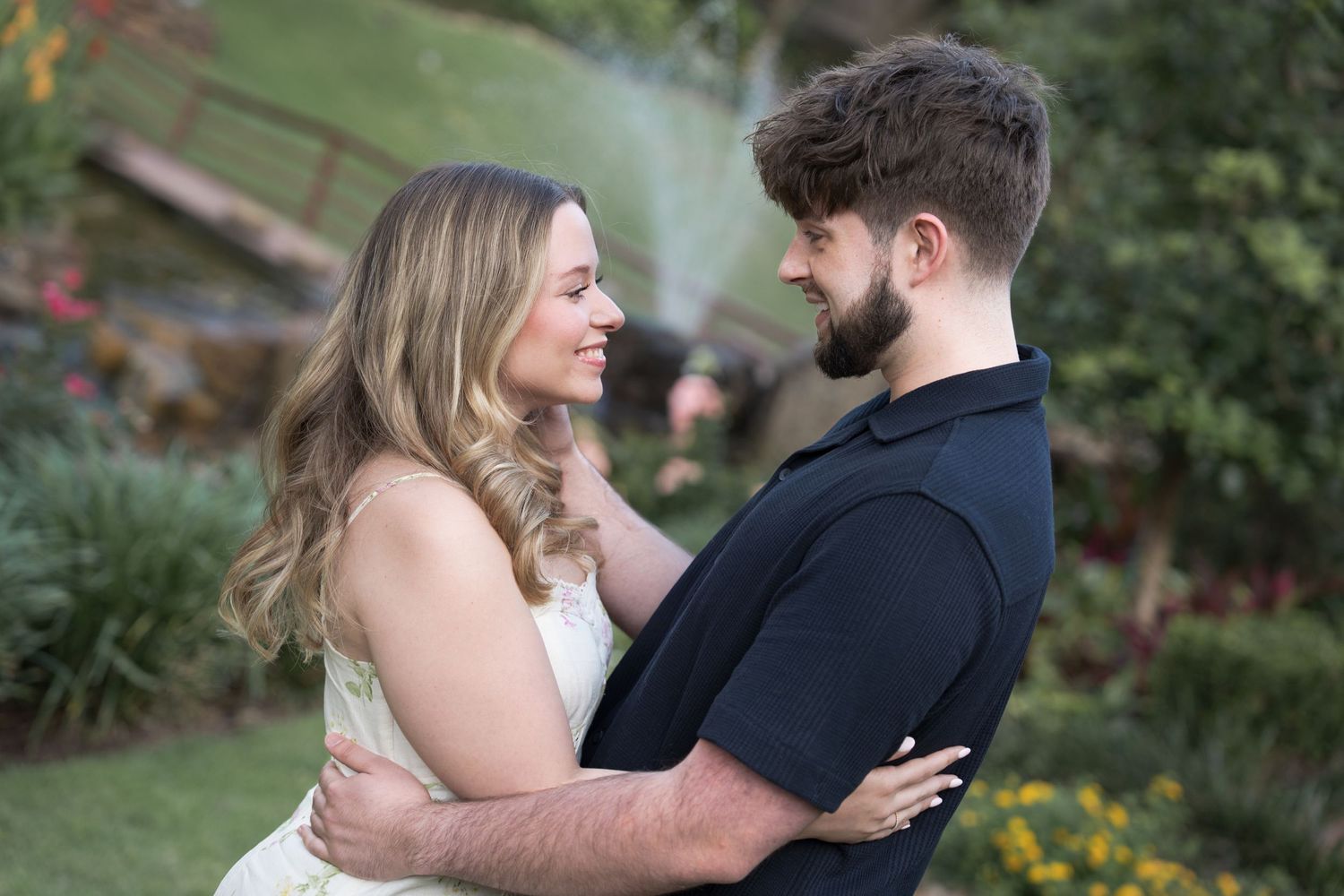 A couple embraces and gazes lovingly at each other in a lush garden setting.