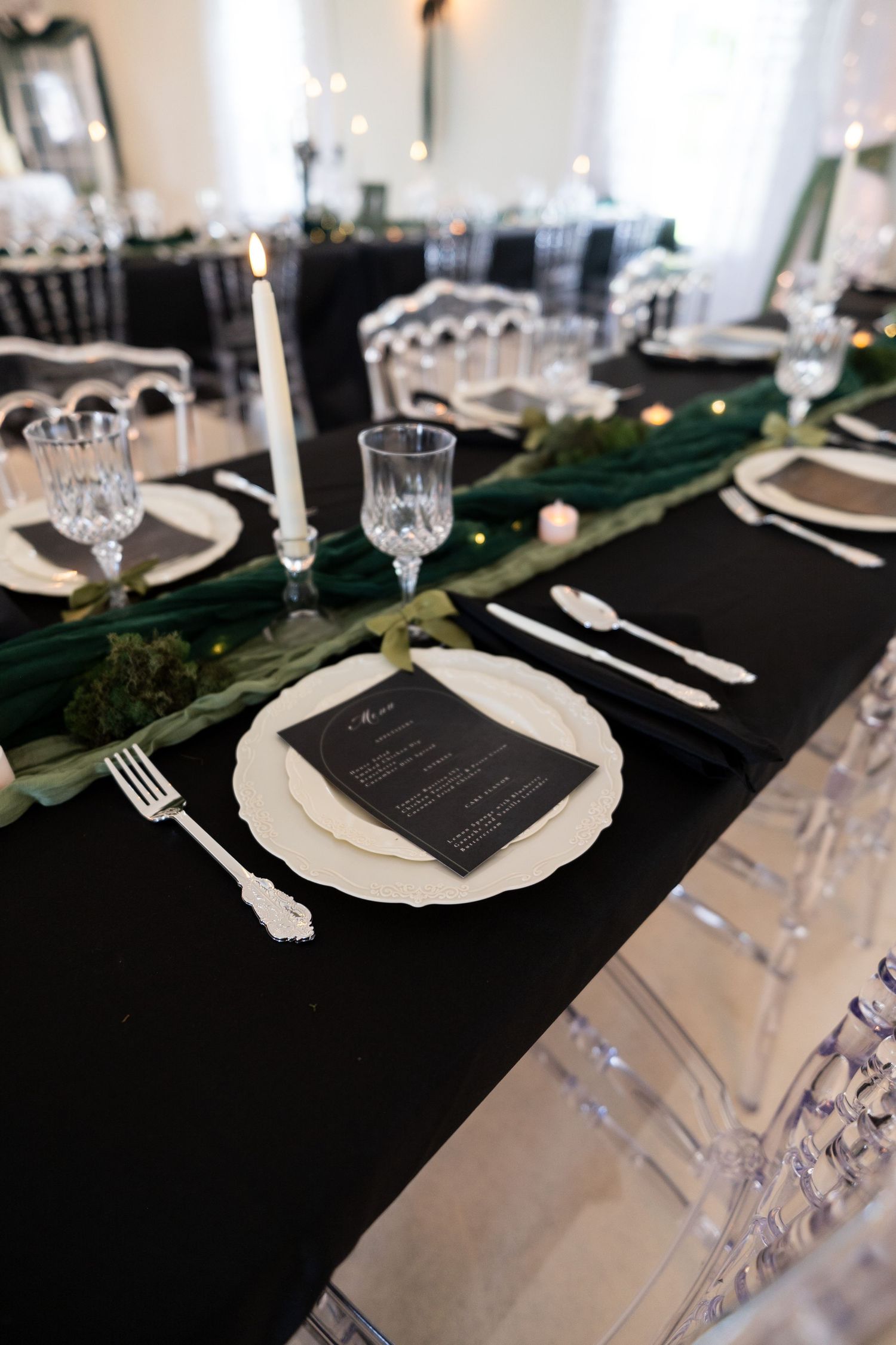 Elegant black and white wedding table setting with crystal glassware, white plates, and green botanical runner.