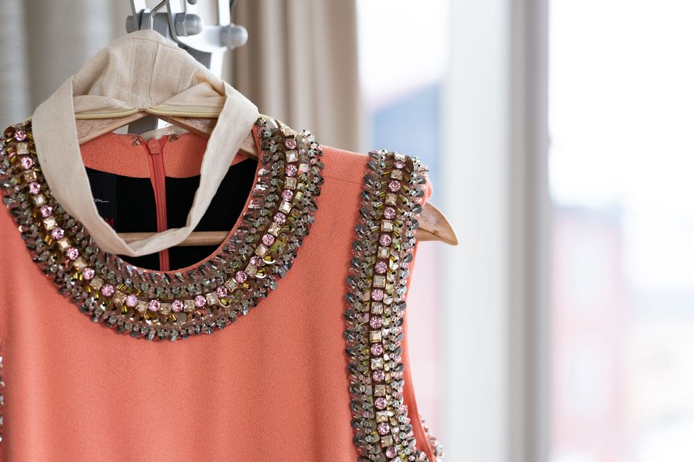 Close-up of a coral beaded neckline dress on a hanger with jewel embellishments.