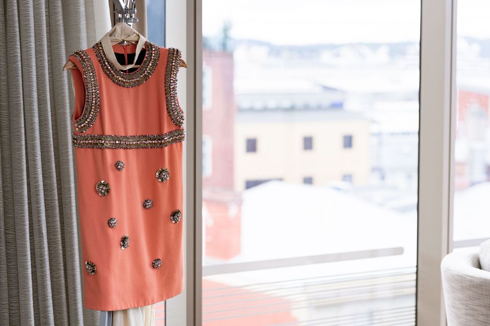Coral embellished mini dress hanging near a window with city views.