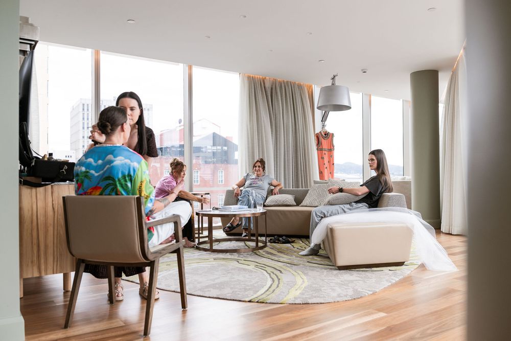 A bright modern living room with large windows where a group of women socialize on stylish sofas and chairs.