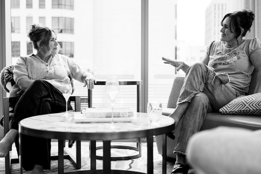 Two women having a conversation in a modern lounge setting, captured in black and white photography.
