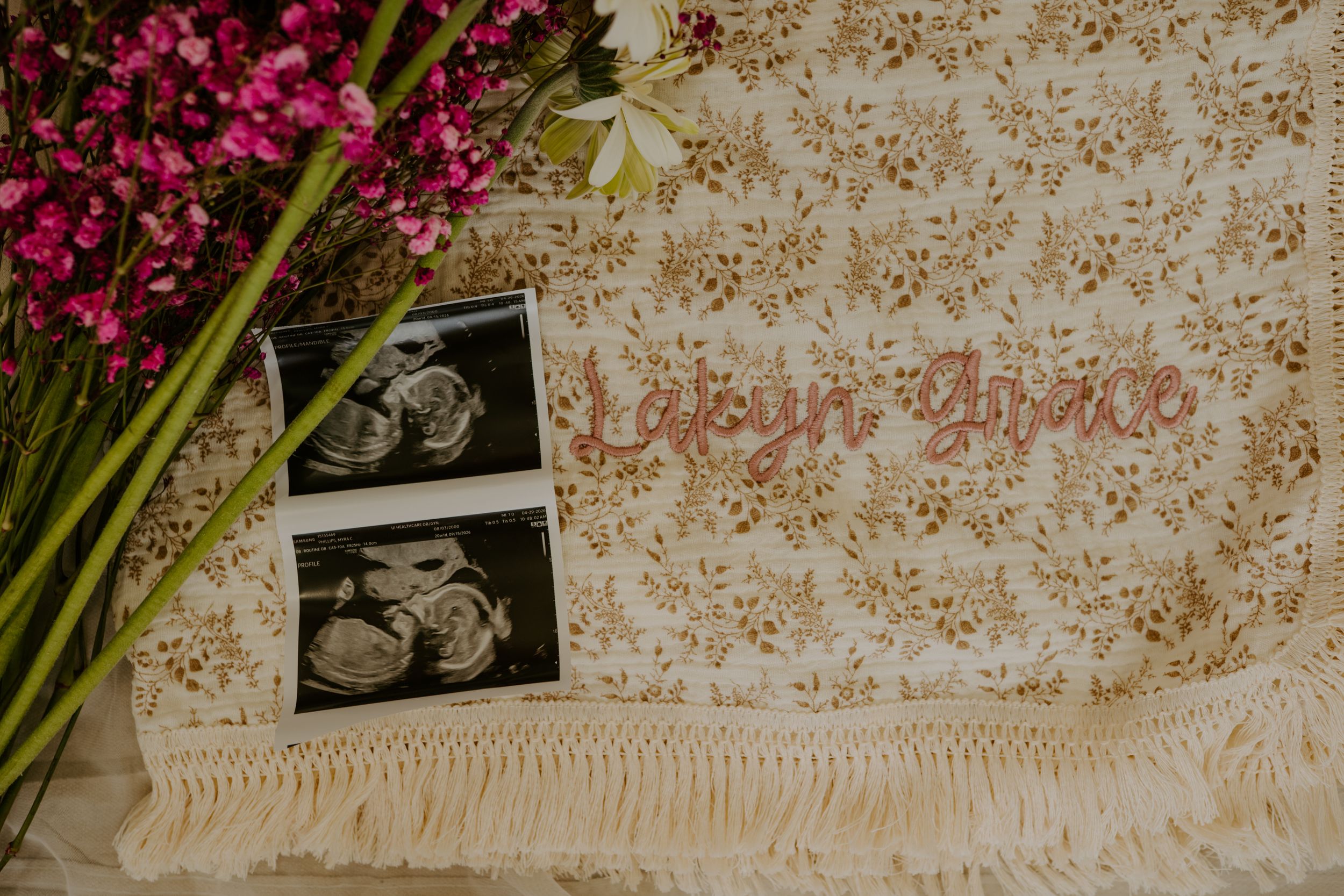 Ultrasound photos and name sign reading Lailyn Grace on floral blanket with pink flowers.