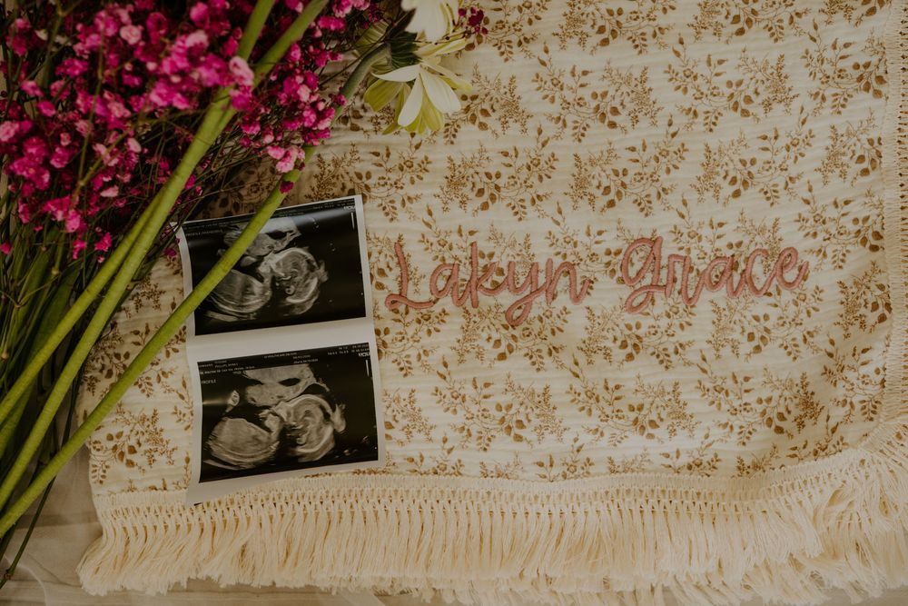 Ultrasound photos and name sign reading Lailyn Grace on floral blanket with pink flowers.