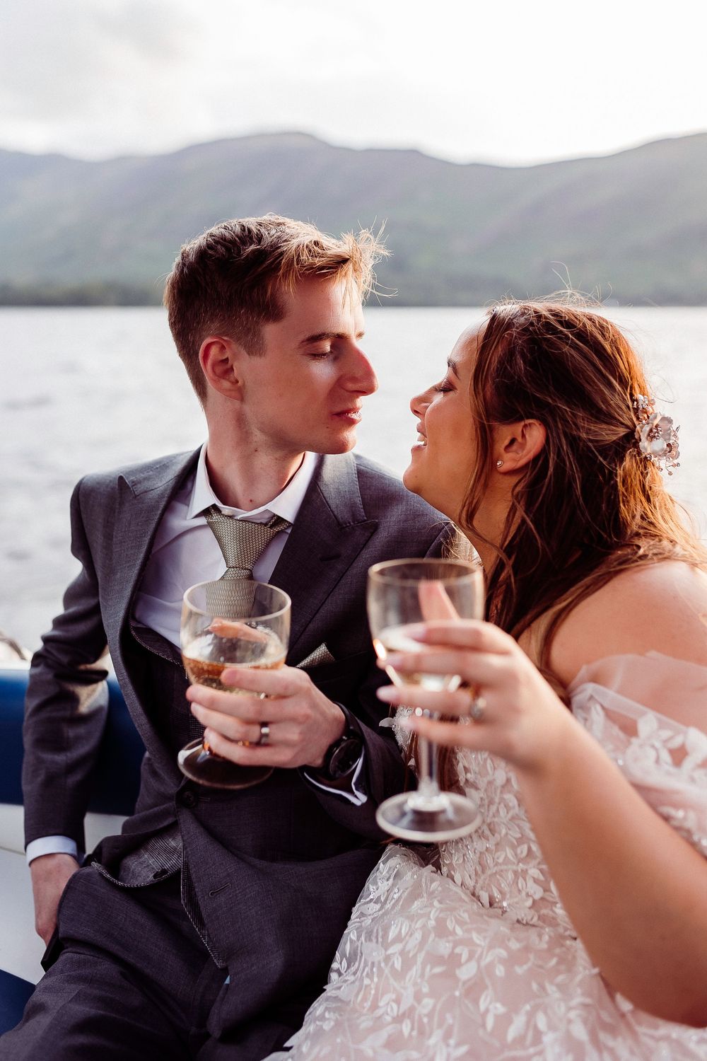 Bride and groom sharing champagne toast on a boat with scenic mountain lake backdrop on their wedding day.