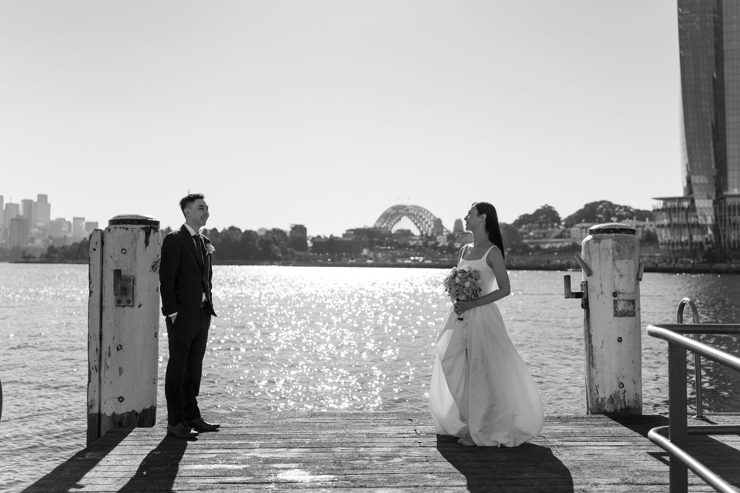 Black and white wedding photo of bride and groom on Sydney Harbour pier with iconic Harbour Bridge backdrop.