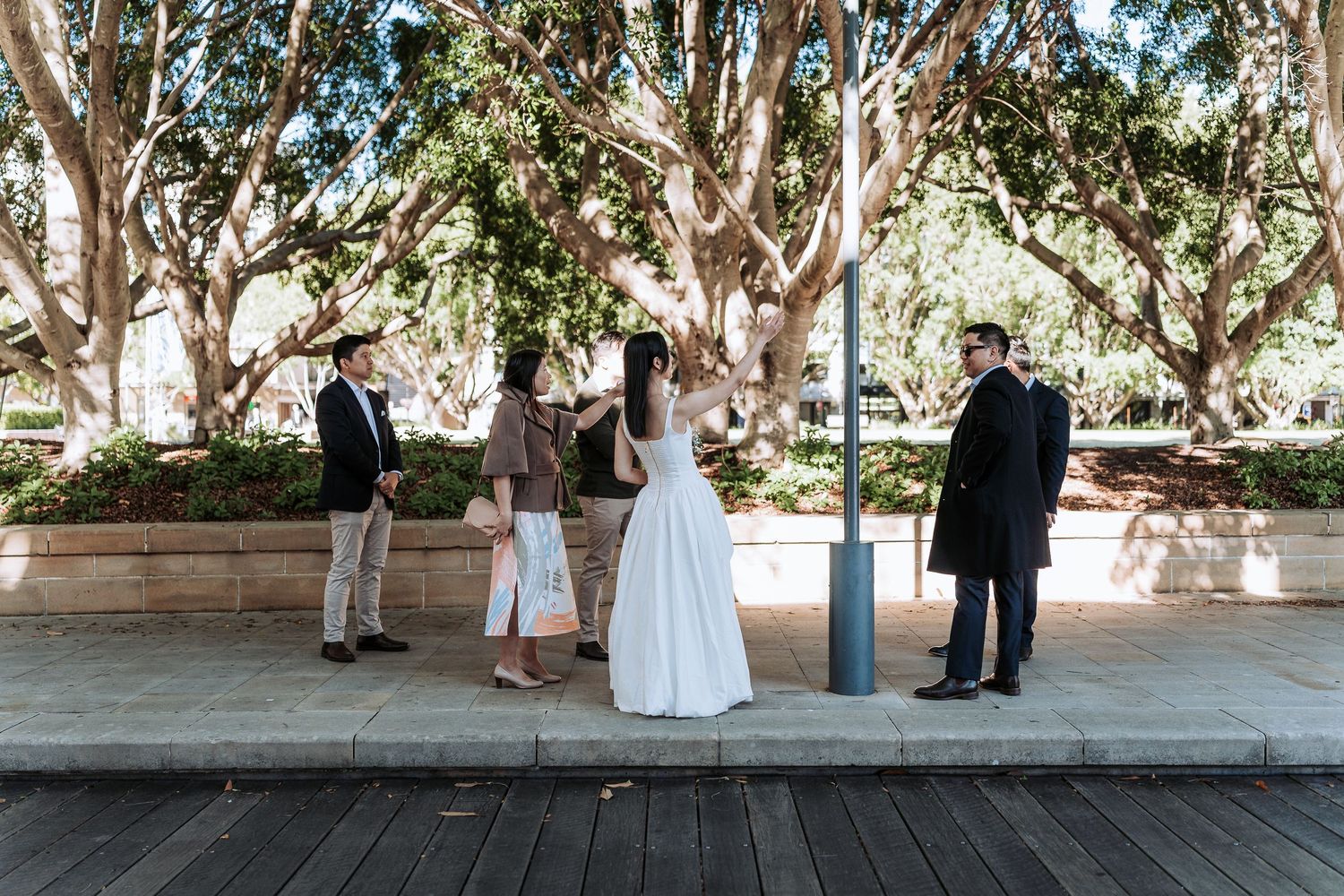 Wedding party gathers outdoors under leafy trees for an intimate pre-ceremony moment in Sydney.