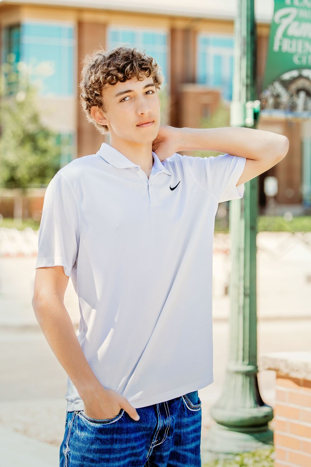 Teen boy in white Nike polo shirt and jeans poses outdoors near a green lamppost on a sunny day in Keller