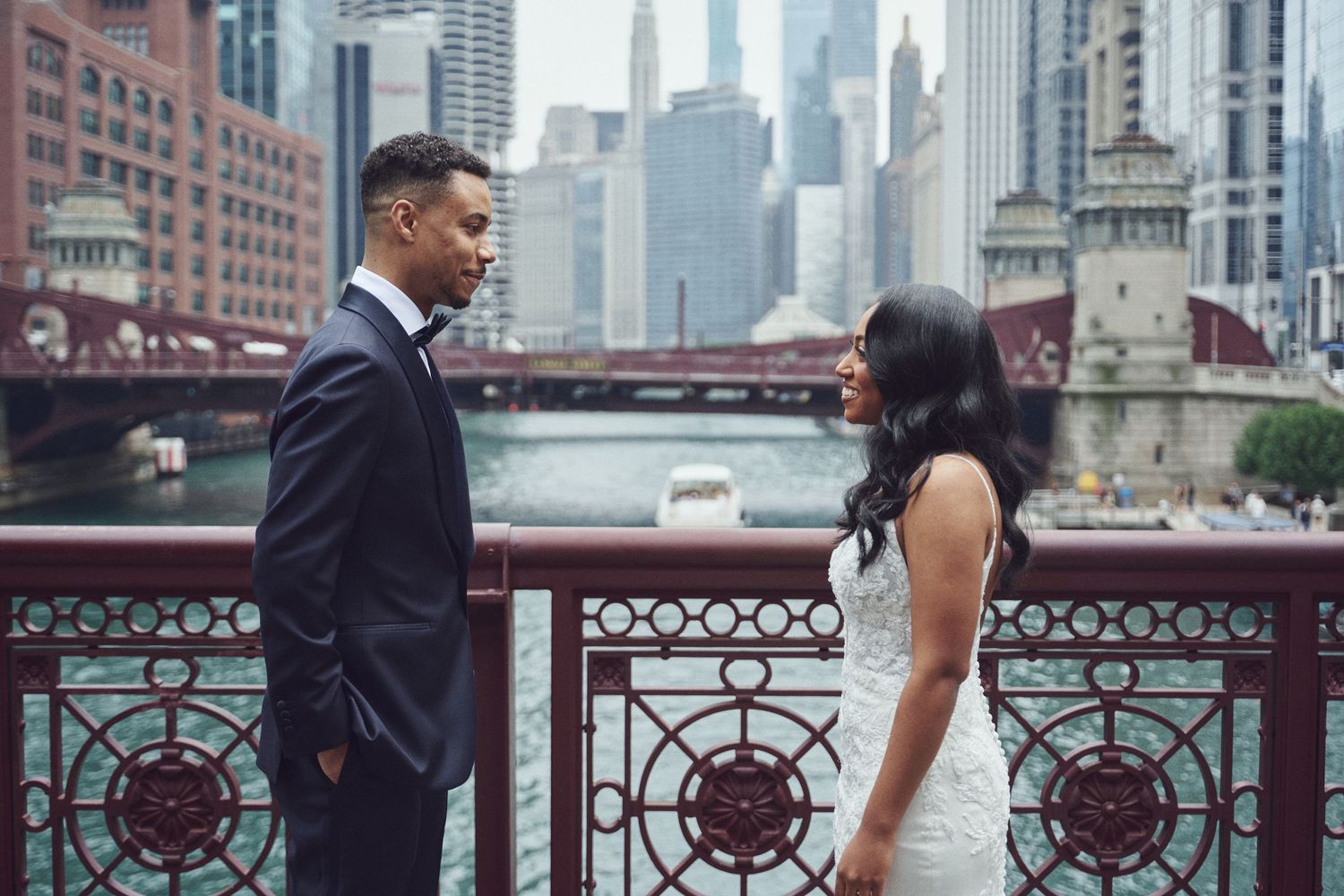 Couple in wedding attire facing each other on a bridge over the Chicago River with city skyline backdrop.