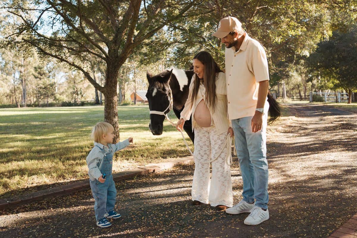 A family with a toddler and pregnant mother poses with a black and white horse in a private property in Sydney during a family photoshoot