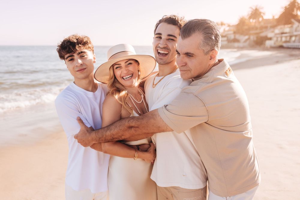 Happy family of four hugging and smiling together on a sunny beach during golden hour vacation.