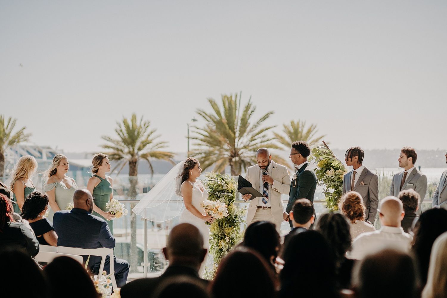 Outdoor beach wedding ceremony with bride and groom at altar, palm trees and ocean in background at The Lane.