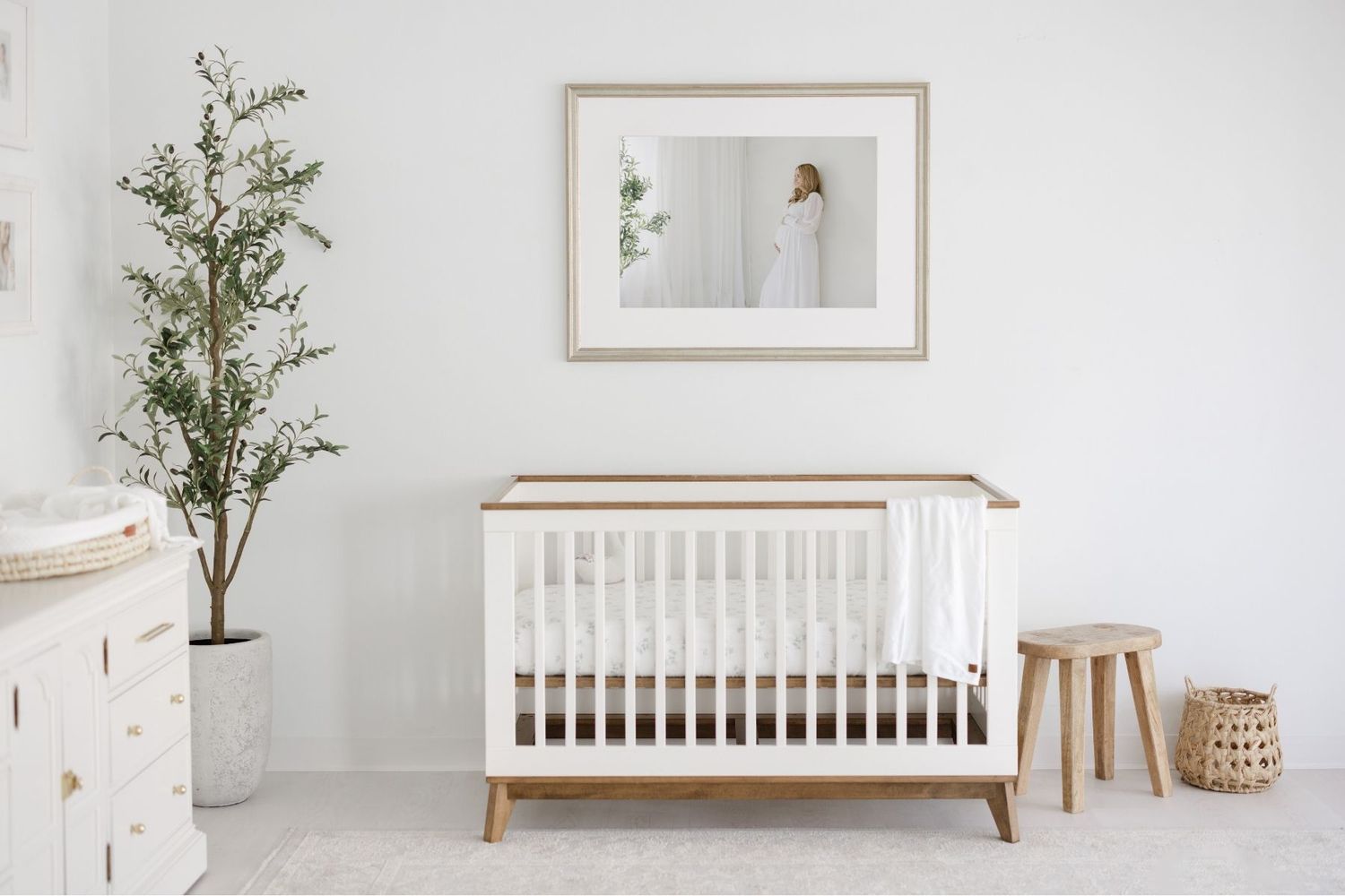 Minimalist Scandinavian nursery design with white crib, potted plant and natural wood accents in a bright room.