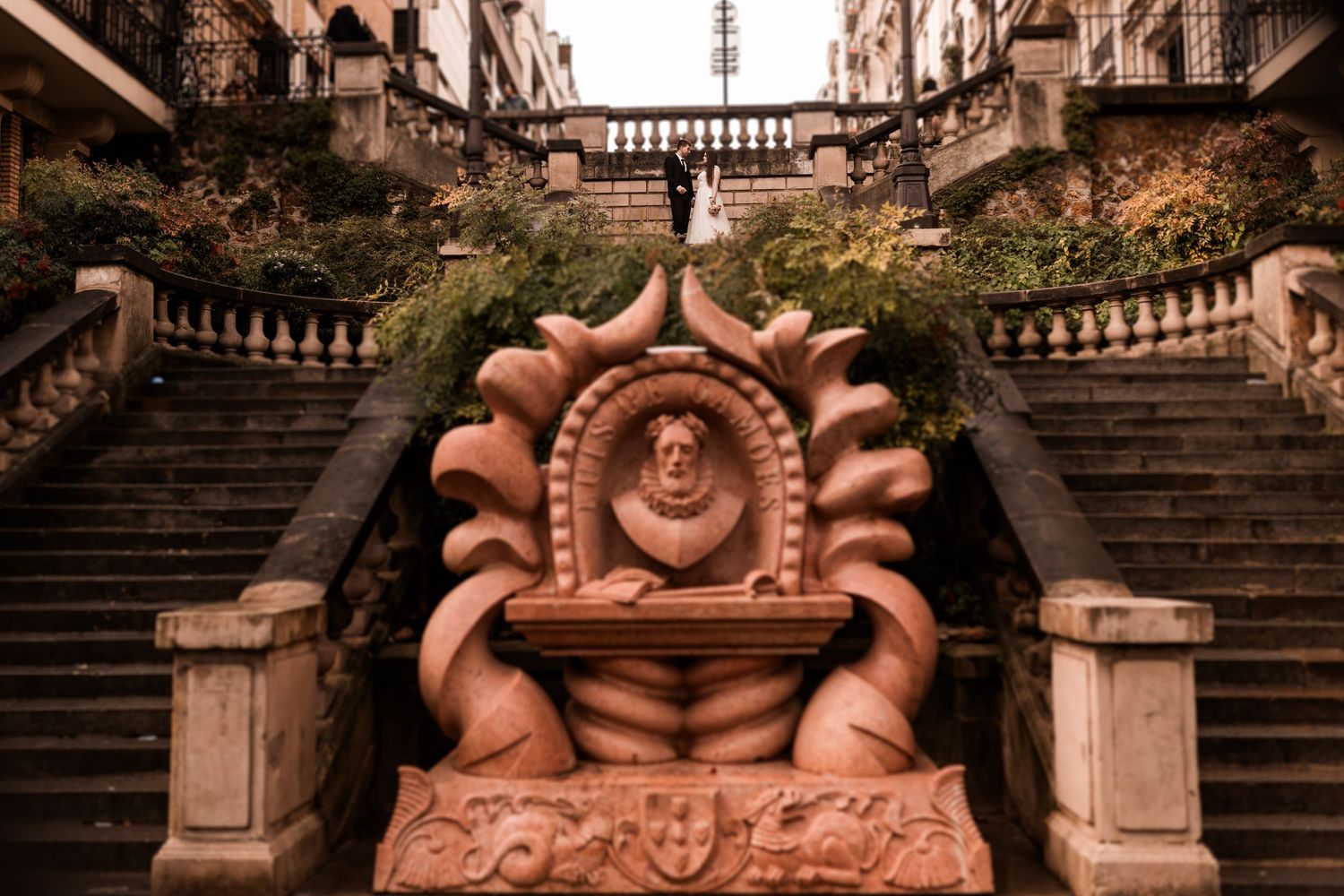 Ornate terracotta fountain sculpture with a bust medallion, flanked by grand stone staircases with balustrades.