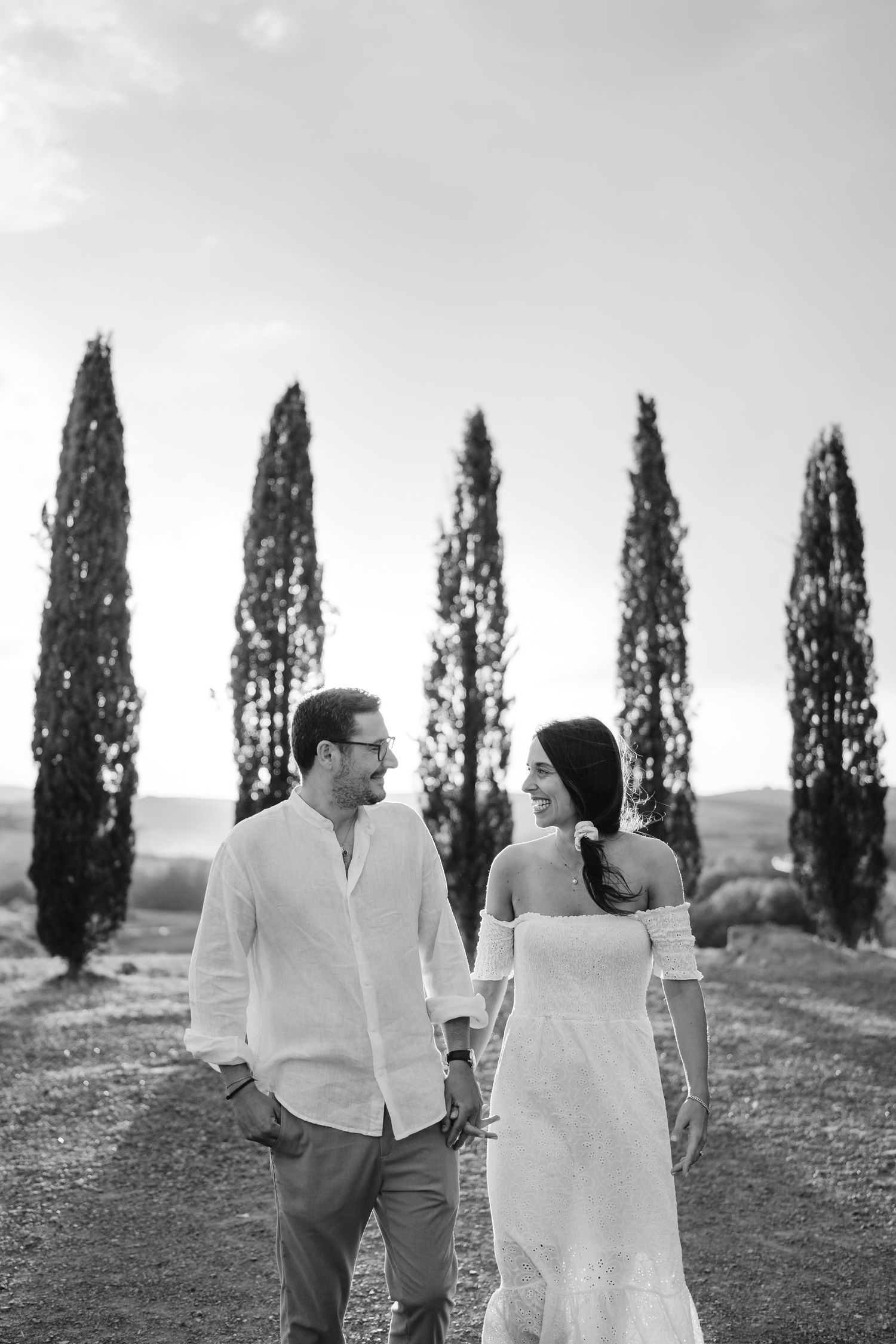 Couple holding hands and smiling while walking through a historic brick alleyway with an arch in the background.