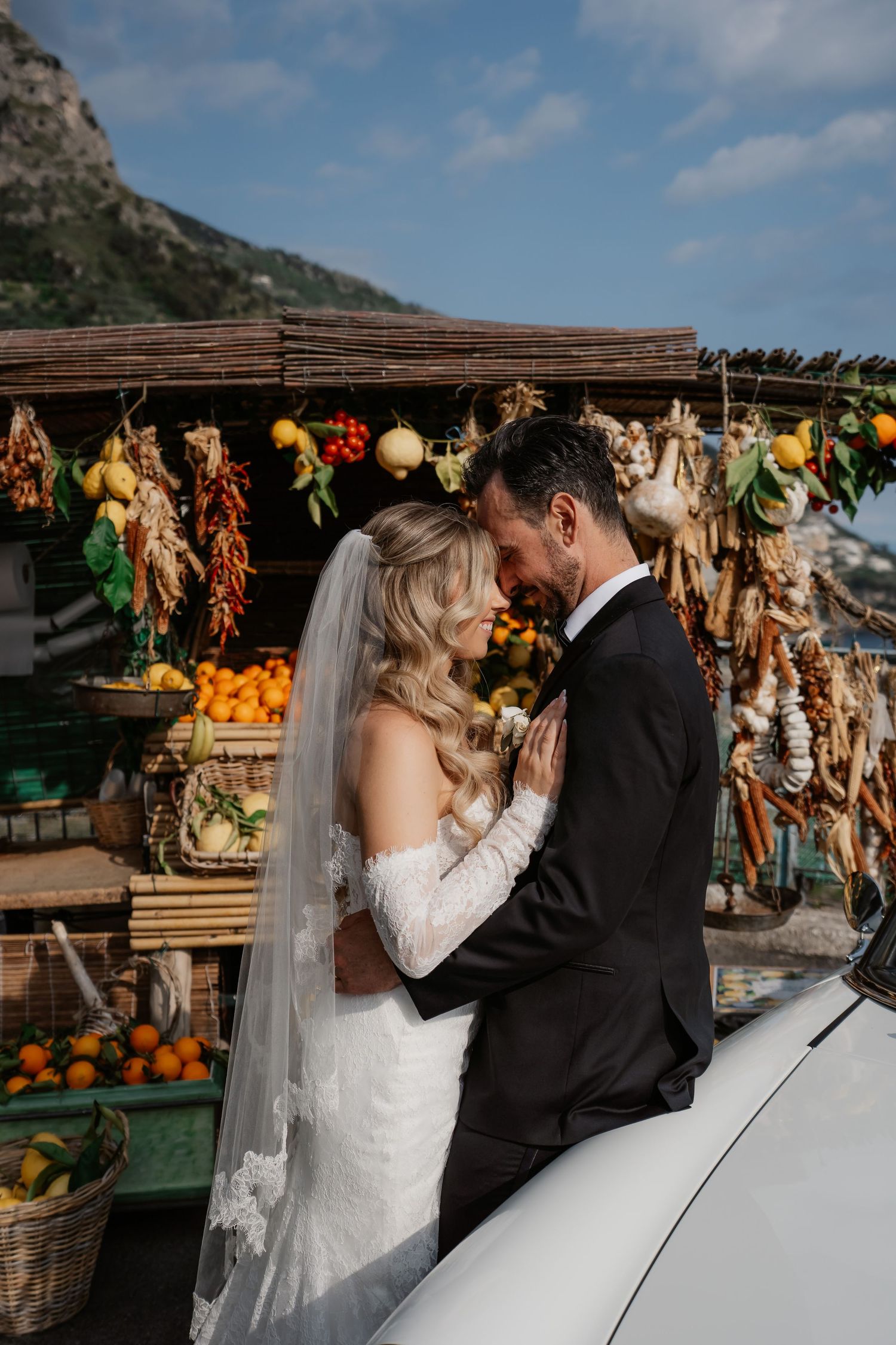 A bride and groom share a romantic moment in front of a colorful Italian fruit market on the Amalfi Coast.