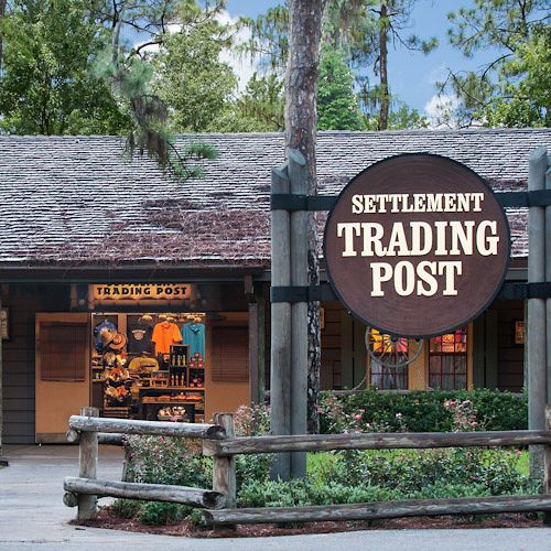 Rustic wooden Settlement Trading Post storefront with sign and merchandise display.
