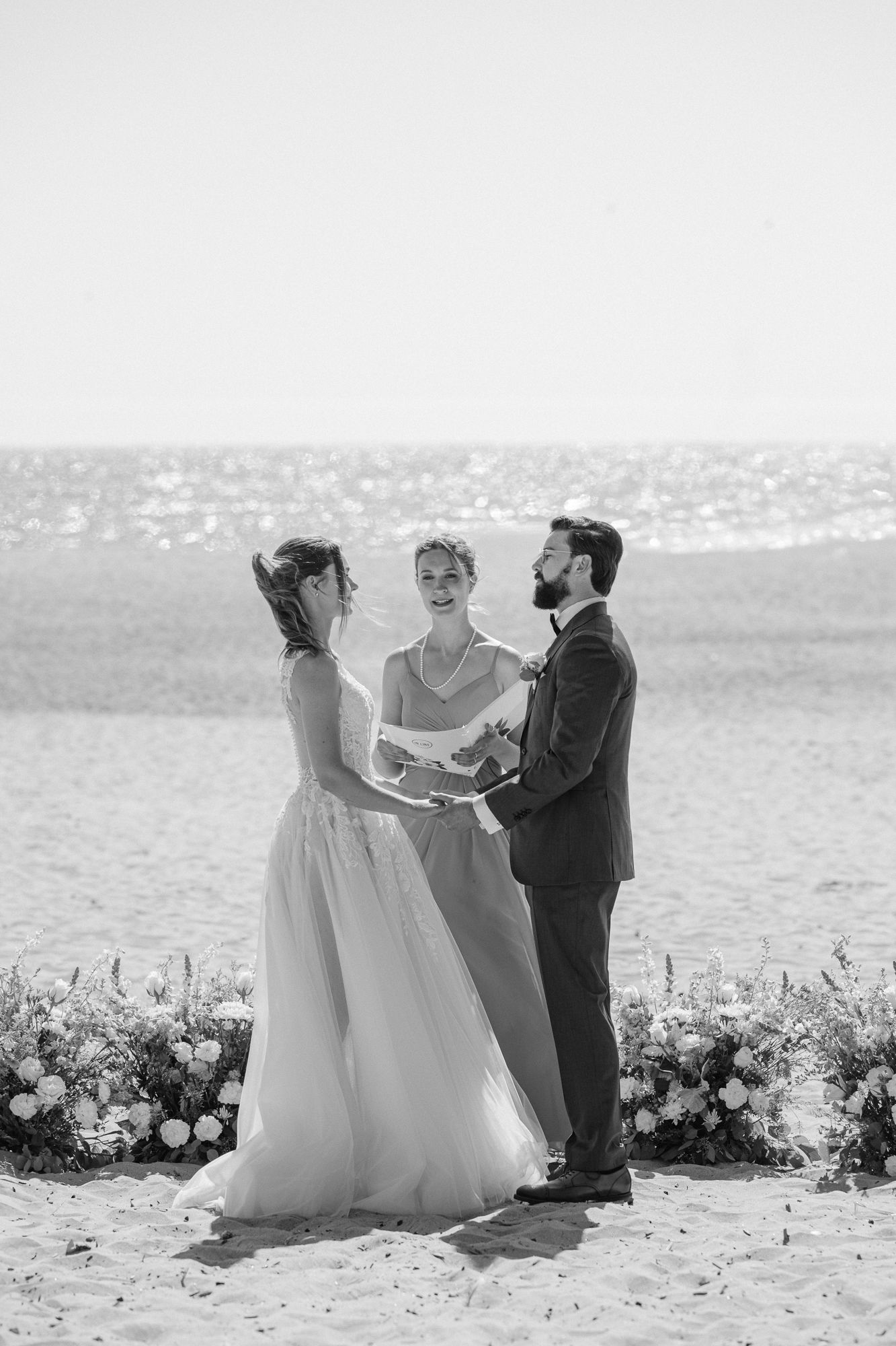 Newlyweds celebrate joyfully with raised arms after outdoor ceremony as wedding party and guests look on.