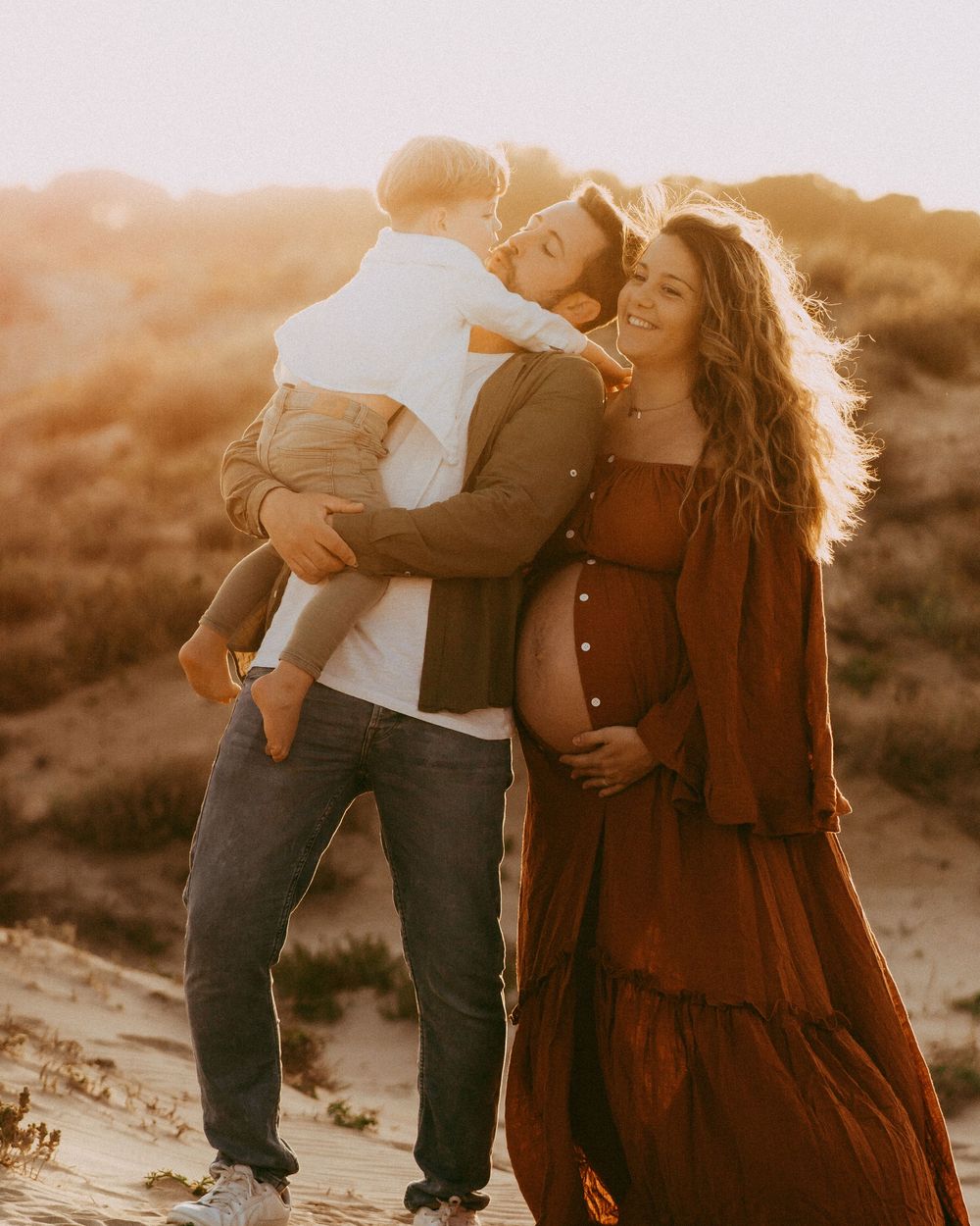 familia con una chica embarazada disfrutando de una sesión de embarazo en un entorno natural al atardecer realizada por María Guerrero