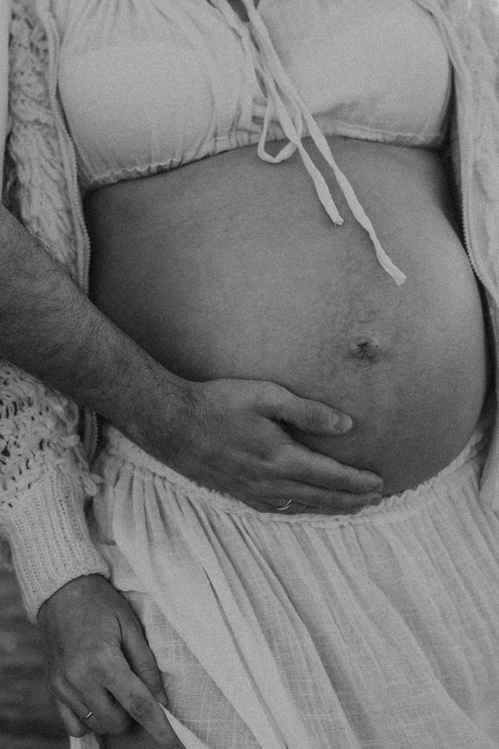 Detalle de la barriga de una mujer embarazada durante una sesión de fotografía de maternidad con luz natural.