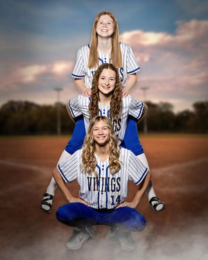 Three girls in Vikings softball uniforms pose in stacked formation on baseball field.